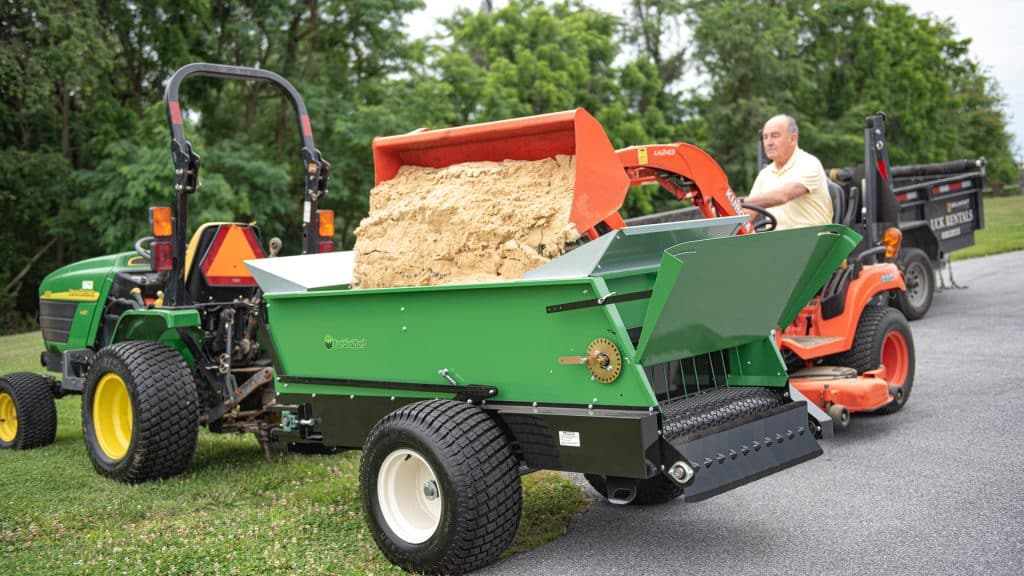 loading a pull behind sand spreader from earth and turf